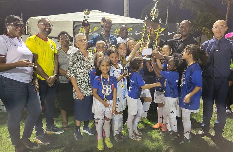 GFF President Wayne Forde hands over the trophy to Marian Academy captain Skylar DeNobrega as her teammates look on.