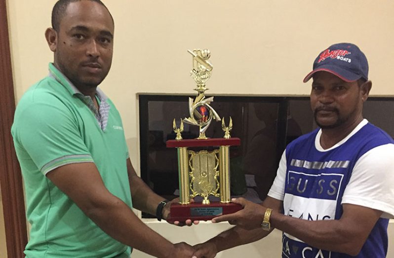West Demearra coach, Dhanpaul receiving the DCB U15 Championship Trophy from newly-qualified umpire Flemroy Lambert