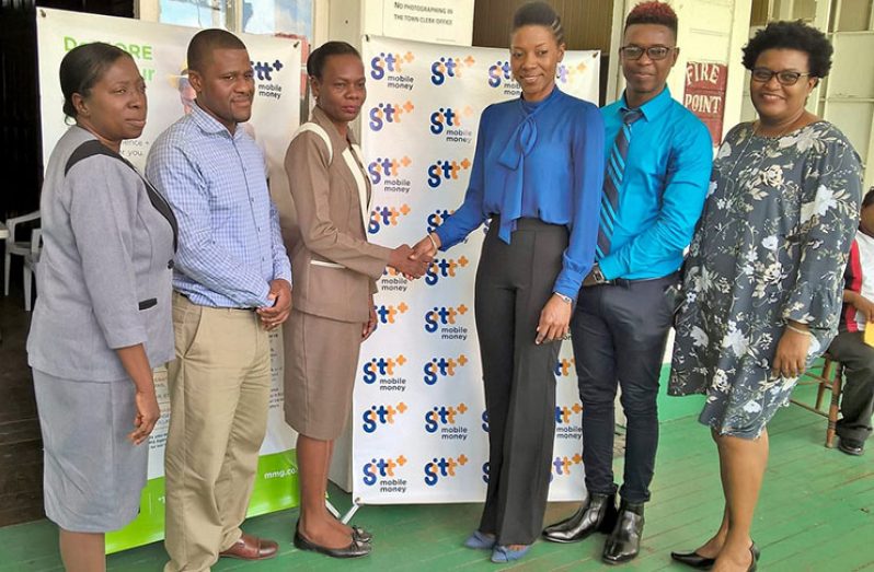 Deputy Town Clerk Sharon Harry-Munroe seals the deal with GT&T’s Vice President/Retail Officer, Tracy Smith.  Also in photo, from left, are: M&CC’s PRO, Debra Lewis, and IT Manager, Adunni Christian; and GT&T’s Mobile Money Specialist, Kester Abrams and PRO, Allison Parker.