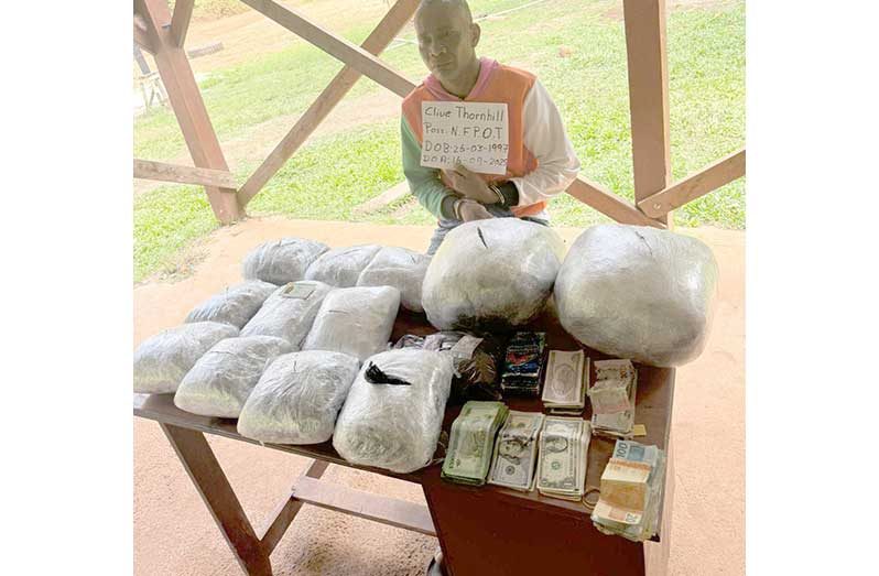 Clive Thornhill was allegedly found carrying a black side bag containing $703,180 in Guyana currency, 1,798 Brazilian Reais, 3,260 Cuban pesos, and US$1,137. Officers then searched two containers Thornhill identified as his property—a white cardboard box and a ten-gallon bucket—inside which they discovered twelve bulky transparent parcels containing leaves, seeds, and stems suspected to be cannabis