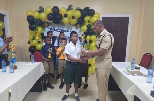 Regional Commander, Senior Superintendent Krishnadat  Ramana, hands over one of the many trophies to one of the champions at the Guyana Police Force Regional Police Division One Annual Spelling Bee Competition 2026, held on Monday
