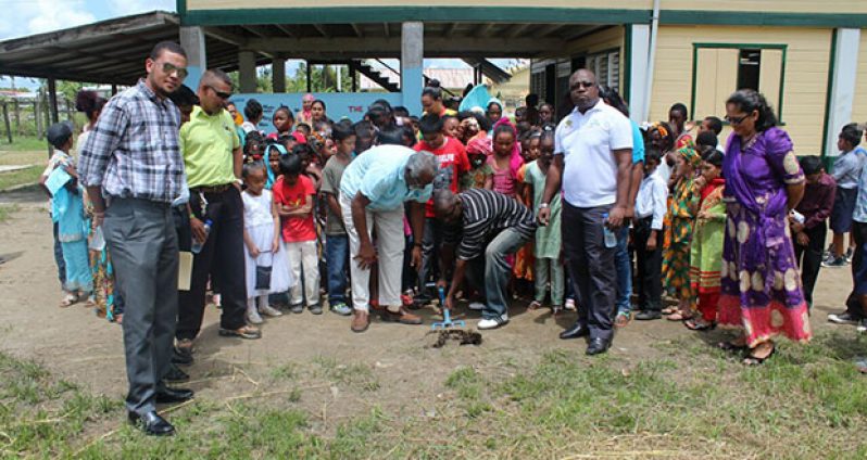 Managing Director (ag) of Guyoil, Reggie Bhagwandin, and Chairman of the Covent Garden Primary School PTA, Junior Cornette, turning the sod as students, teachers and representatives of Guyoil look on