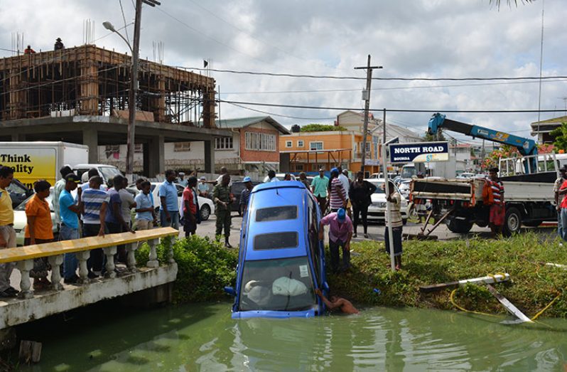 Tow truck representatives trying to attach a hook onto the front of the vehicle to extract it from the canal while others look on