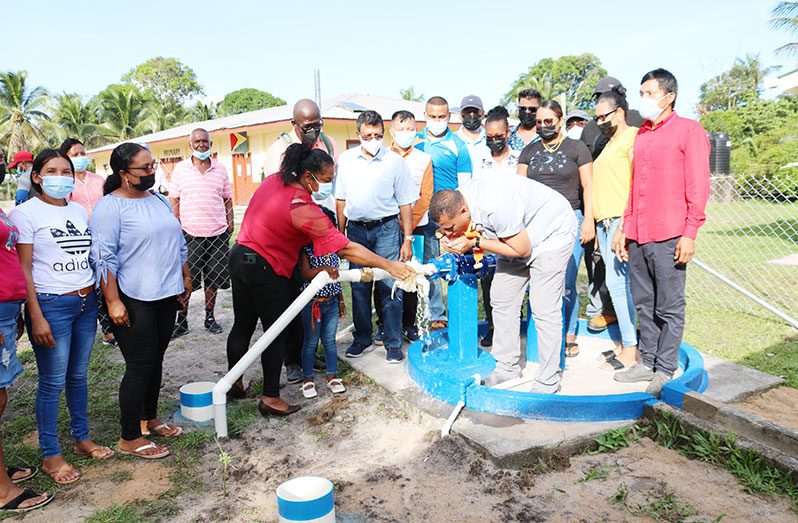 Minister Croal is flanked by residents and other officials as he samples the water from one of  River's View wells (GWI photo)