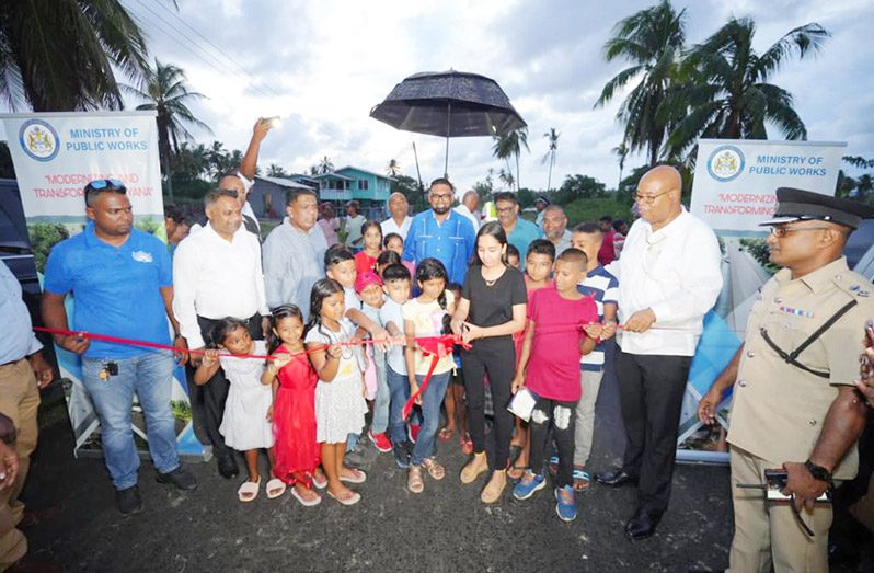 Public Works Minister Bishop Juan Edghill assisting in the cutting of the ceremonial ribbon for the
opening of the #58 Village farm-to-market access road as Minister within the Public Works Ministry
Deodat Indar, Agriculture Minister Zulfikar Mustapha, and President, Dr. Irfaan Ali and others look on
(Office of the President photo)