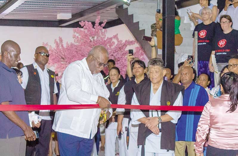 Prime Minister, Brigadier (Ret'd) Mark Phillips cuts the ribbon to open the Master Frank Woon-A-Tai Budokan in the presence of Master Woon-A-Tai yesterday. (Shaniece Bamfield photo).