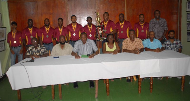 The victorious Demerara Cricket Club first division team, who are out decked in their limited overs tops, strike a pose with the GCA/Hadi’s Mall Inc. first division trophy while displaying their medallions, even as the members of the head table sit in forefront. Third from left is GCA’s president Roger Harper, who has Percy Hedwig on his right. (Photo by Sonell Nelson)