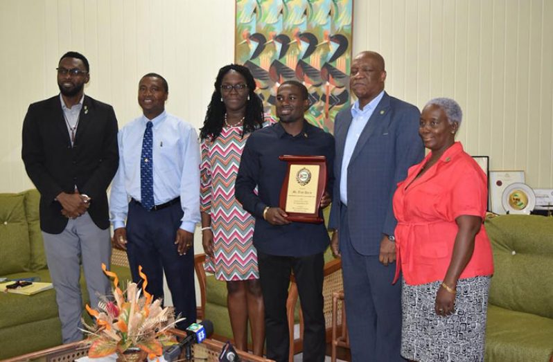 Troy Doris is handed a plaque of achievement from Minister of State Joseph Harmon in the presence of Director of Sport Christopher Jones (first from left), Permanent Secretary of the Ministry of Public Service, Reginald Brotherson (second from left) and other MoTP staff.