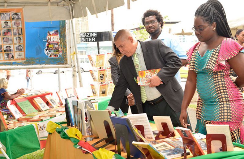 Minister of Social Cohesion, Dr. George Norton takes a closer look at books displayed at the Literary and Visual Arts Street Fair.