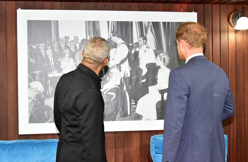 President David Granger shows Prince Henry of Wales an image of his cousin Prince Edward, Duke of Kent, who presented the instruments of Guyana's independence to former Head of State and then Prime Minister, Forbes Burnham.