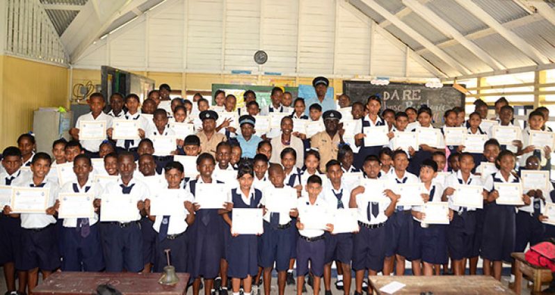 The students, posing with their certificates of completion for the DARE project, are flanked by Commander Stephen Mansell, Head Teacher Shivaughn Cadogan, and officers of the GPF