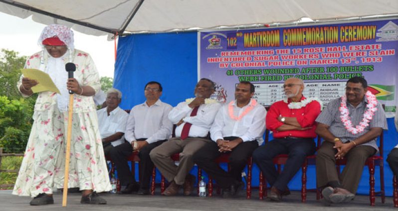 An elderly woman reciting a dramatic poem on stage, capturing the undivided attention of President Donald Ramotar, Prime Minister Sam Hinds, Region 6 Chairman David Armogan, Minister of Culture, Dr. Frank Anthony, BHRA Head Dr. Vishwa Mahadeo and Mr. Deobajan