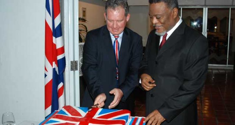Prime Minister, Mr Samuel Hinds awaits his turn as British High Commissioner Mr. Andrew Ayre has the first go at cutting the traditional birthday cake in celebration of Queen Elizabeth II’s 88th birthday