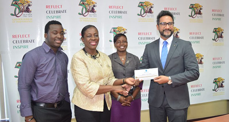 Javier Marks of Guyana Music School stands next to Minister within the Ministry of Education, Nicolette Henry, as she receives a cheque from Managing Director of Republic Bank (Guyana) Limited, Richard Sammy