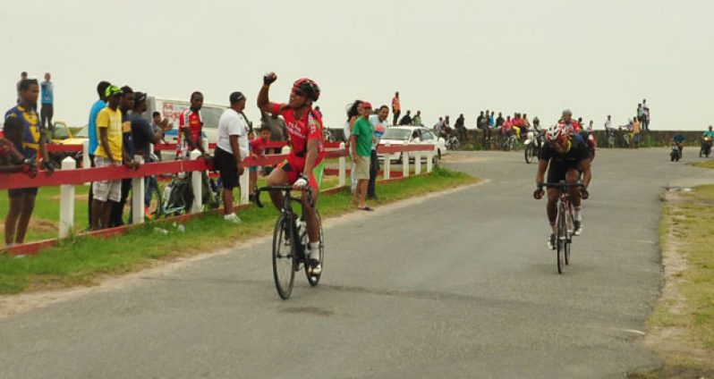 Alonzo Greaves (left) raises his hand in triumph as he crosses the finish line to win the feature 30-lap race of the George Cumberbatch memorial cycle meet. At right is Geron Williams finishing second. (Sonell Nelson photo)
