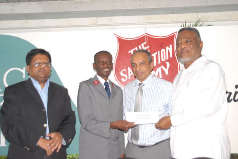 Prime Minister Hinds presents the cheque to Divisional Commander Emmerson Cumberbath, while Finance Minister Dr Singh (at left) and Mr. Edward Boyer look on