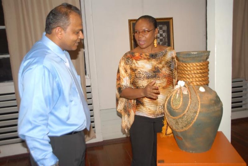 Artist Jennifer Gibson explains her piece, “Two Faced”,  to the Minister of Culture, Youth and Sport, Dr. Frank Anthony.