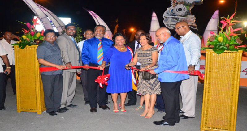 Helping First Lady, Mrs Deolatchmee Ramotar (third right) with the symbolic cutting of the ribbon to formally declare the exposition open are, from left: Finance Minister, Dr. Ashni Singh; Tourism Minister (Ag), Mr. Irfaan Ali; Agriculture Minister,  Dr. Leslie Ramsammy; Prime Minister, Mr, Samuel Hinds, and his wife, Mrs Yvonne Hinds; Private Sector Chairman, Mr. Ramesh Persaud (partially hidden); President Donald Ramotar; and Minister within the Finance Ministry, Bishop Juan Edghill