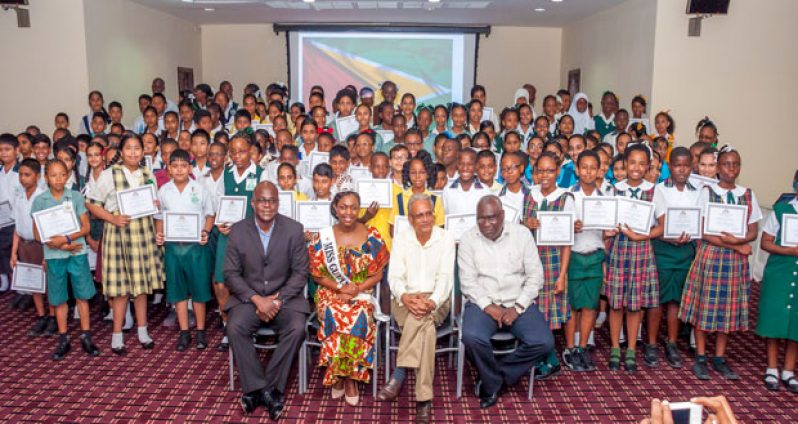 ‘CONGRATULATIONS!’  In photo, from left, are Chief Education Officer Mr Olato Sam along with Miss Guyana United Kingdom, Zena Bland; Minister of Education Dr Rupert Roopnaraine; and chairperson of the ceremony ACEO (Primary) Mr Marcel Hutson, posing with the Top 1% students who excelled at the recent NGSA exams (Delano Williams photo)