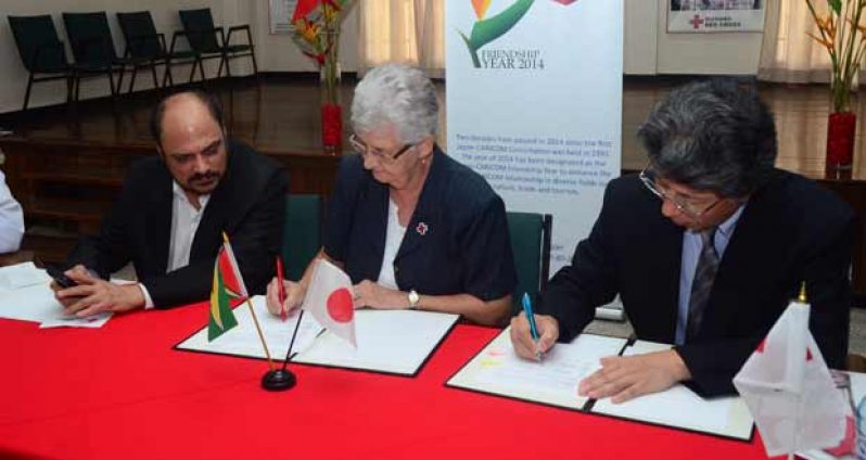 The Red Cross’ Mrs Dorothy Fraser and Japan’s Mr Yoshimasa Tezuka append their signatures to the Grant documents. At left is Health Minister, Dr Bheri Ramsarran (Photo by Adrian Narine)