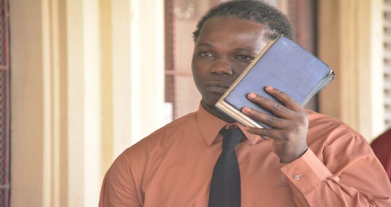 The chained accused, Orin David, called ‘Plait Hair’ seen on his way to court yesterday, when he tried to hide his face with a book.