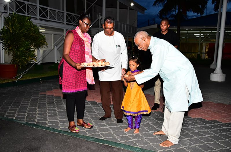 President David Granger helps his granddaughter, Faraa, place a diya at the 2017 Diwali Utsav held at the Baridi Benab, State House.
