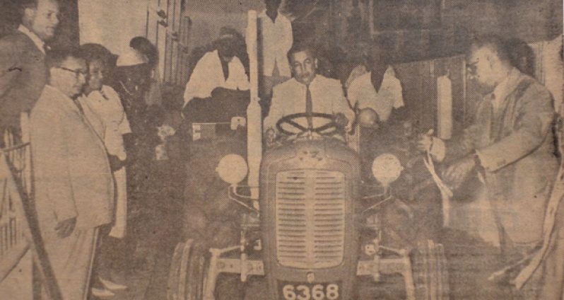 A step forward:  Mr Randolph Cheeks, Minister of Local Government, cuts the ribbon, and the new $4,600 tractor and trailer acquired by Lodge Village Council is set in motion. It was intended to be used to collect garbage in the village. (January 6, 1966)