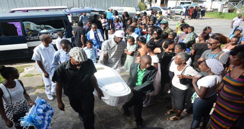 Mourners and other residents look on as Jadon’s body is taken from the hearse into the church