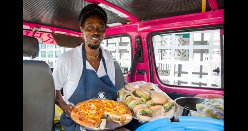 Keith Hutchins, popularly known as “Ras” poses with some of the Ital delicacies he sells on the street in his bus every day at the Rubis Gas Station on Vlissingen road, Georgetown