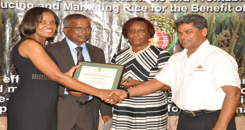 Ms. Sharonmae Shirley hands over the award to Chairman of the Board of Directors of the GRDB, Mr. Badrie Persaud, in the presence of Mr. Singh and Ms. Allison Peters