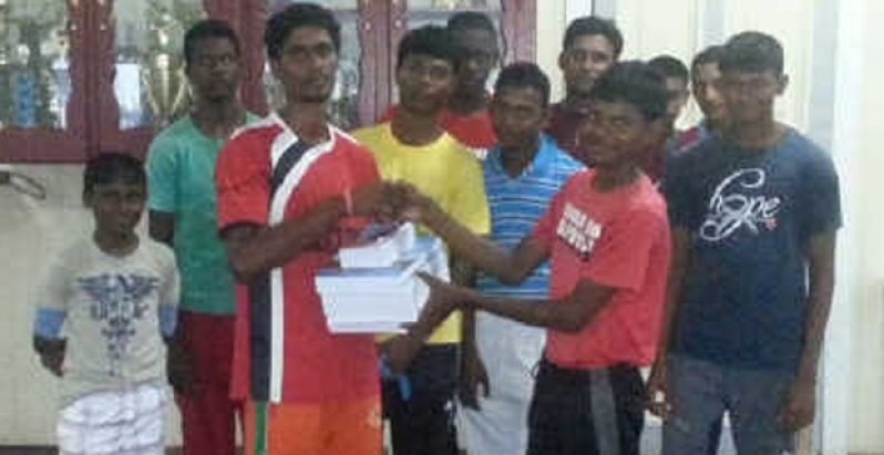 PMCC Under-17 skipper Daniel Samaroo (forefront right) is all smiles as he accepts his textbooks from Yogendra Harrinarine, in the presence of other club members.