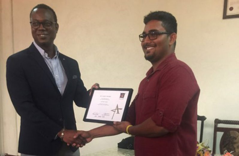 Devesh Persaud of the Nand Persaud Group of Companies receives the award from G & A Communications Inc Managing-Director, Devin Griffith