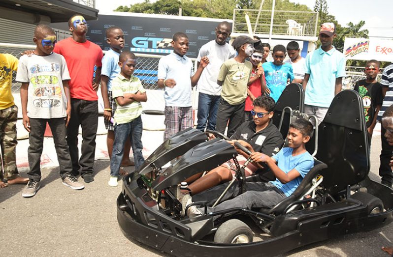 125cc competitor Mikhil Persaud shows one of the children how to use the kart. (Adrian Narine photos)