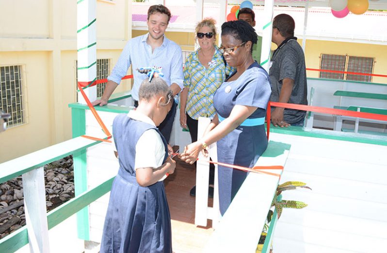 A student of Hackney Primary School cuts the ceremonial ribbon at the entrance of the dining hall in the presence of headmistress Verna Naomi Jack and Pomeroon Trading CEO, Duncan Turnbull (left standing), among others guests