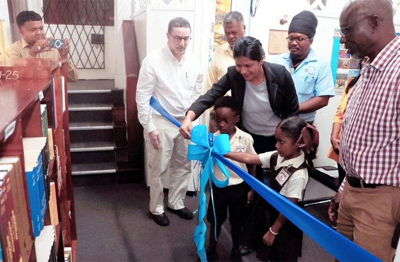 Two students from the Comenius Primary cutting the ribbon to officially launch the library, with Chairman of the ERC, Shaykh Moeenul Hack (left), Deputy Chairman Mr. Charles Ogle, CEO Ms. Gomin Camacho, Commissioners Mr. Deon Dick (Ras Khafra) and Mr. Norris Witter (right), among others, looking on.