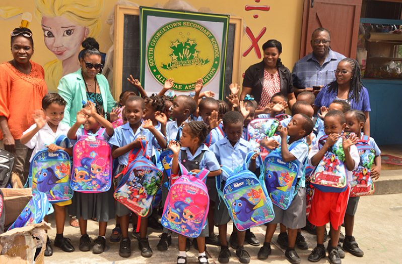 St. Stephen’s Primary School’s teachers and South Georgetown Secondary School Alumni smile with the cheerful students of St. Stephen’s Primary as they hold their brand new book bags.