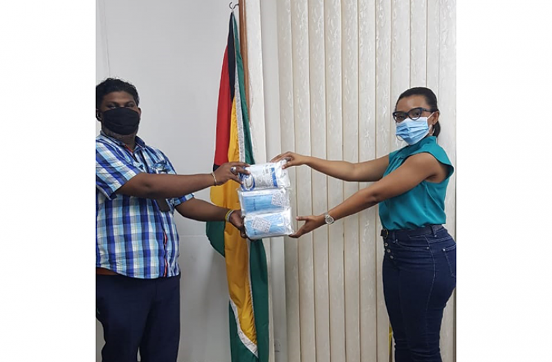 Personal Assistant to Minister Catherine Hughes, Cathy Martin, presents the masks to Kristopher  Roberts, Liaison Officer of the National Community Policing Organisation of Guyana, at the Ministry of Public Security