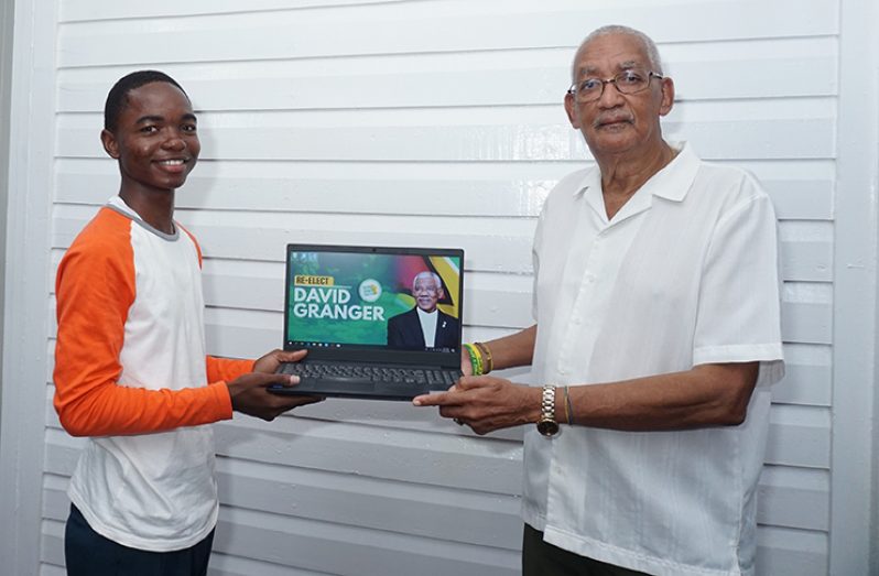 Presidential Adviser, Dr. Mark Kirton presenting Joshua Edward with a laptop