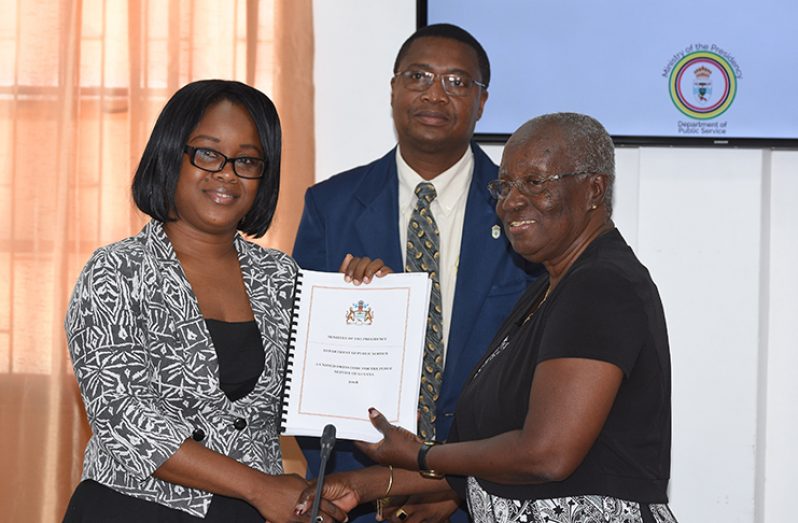 Cheryl Sampson receives the report from Committee chair Akilah Doris on behalf of Minister of the Public Service, Dr Rupert Roopnaraine, while PS of the ministry, Reginald Brotherson, looks on. (Samuel Maughn photo)