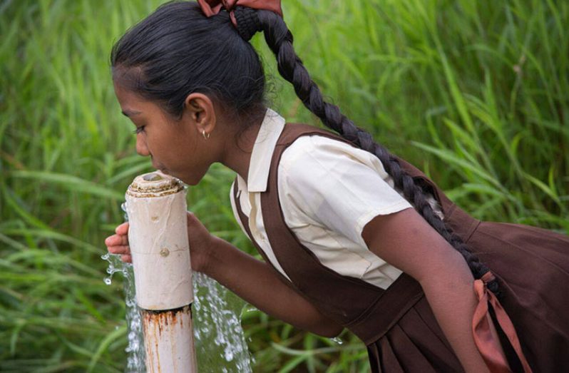 A pupil of Dora Primary School on the Soesdyke-Linden Highway drinks water from a broken pipe (Samuel Maughn Photo)