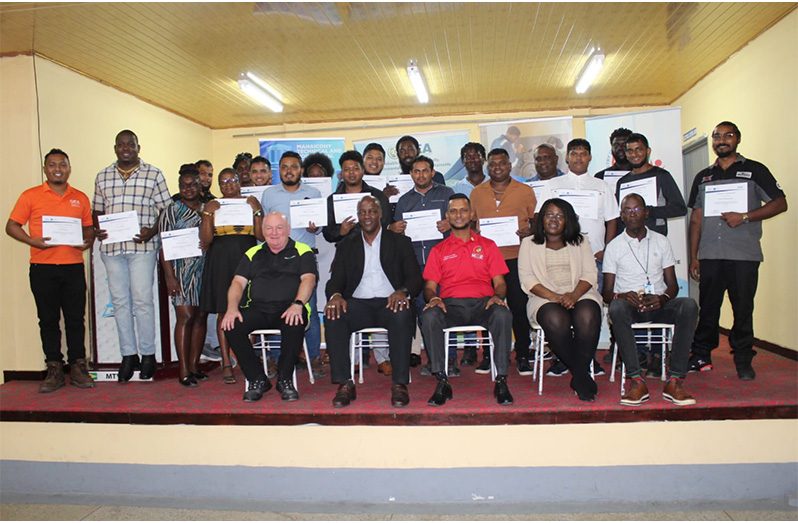 (From left to right) Mr. Steve Burr, Senior Trainer and Director, REVAMP Training Limited; Dr. Alfred King, Permanent Secretary, Office of the Prime Minister; Dr. Ritesh Tularam, Deputy Chief Education Officer (Technical) Ministry of Education; Ms. Shevon Wood, Deputy Chief Executive Officer, Guyana Energy Agency; Mr. Collis Best, Administrator, Mahaicony Technical and Vocational Education Training Centre along with participants who completed the fourth EV Maintenance and Repairs Training Programme