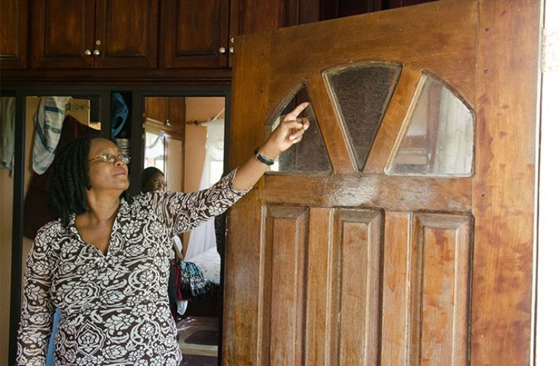Evelyn Estwick lived through the troubled times, during which, her nephew Joslyn Jones went missing. In this photo, she points to a section of her bedroom door where a bullet passed through. The broken glass on the door serves as a memory of the past they wish never to repeat. 
Photos by Delano Williams