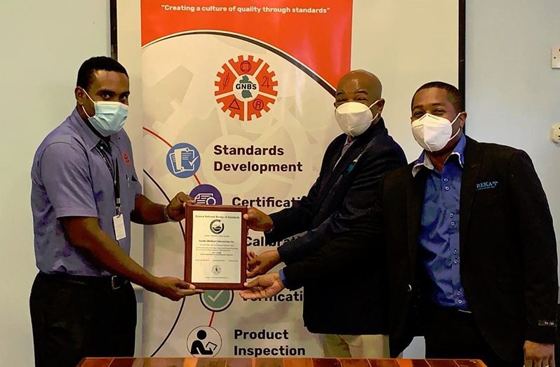 GNBS Technical Officer, Keon Rankin, hands over a plaque to Director of Eureka Medical Laboratories Inc., Edward Boyle on April 20, 2021
