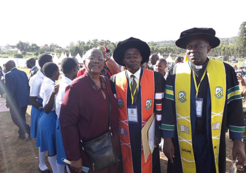 Dr. Joy Agard-Mighty in Uganda with Academic Registrar Mr Magara Silver and Vice-chancellor Rev. Fr. Dr. Deus Karemire (Students in the background)