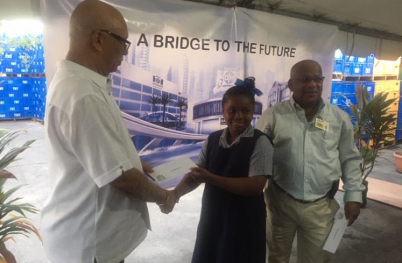 BANKS DIH Chairman, Clifford Reis hands over a cheque to a student of the Ithaca Primary School, West Bank Berbice, for the funding of a school project, as the Berbice Branch Manager Reginald Matthews looks on (Photograph by F.Q. Farrier)