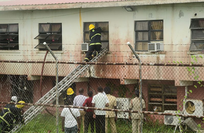 A firefighter tries to gain access to one of the Eve Leary offices in the presence of senior police ranks, during the fire on Monday (Adrian Narine photo)