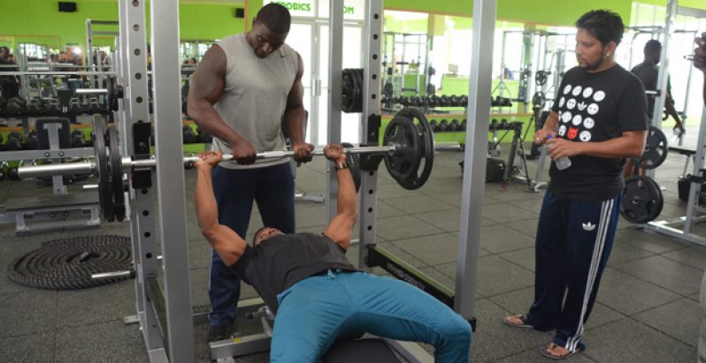 Sarwan watches on as two of the trainers demonstrate bench-pressing. (Delano Williams Photo)