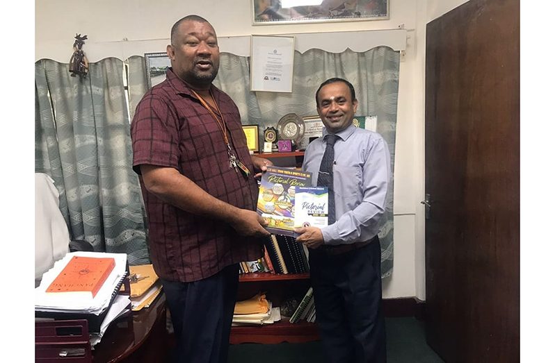 RHTYSC Secretary, Hilbert Foster, presents a copy of the club magazine to the Director of the Tain Campus of the University of Guyana.