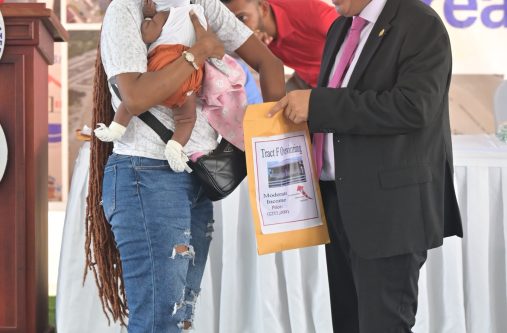 A mother holding her child pulls her lot number from an envelope being held by Minister of Housing and Water, Collin Croal, at the two-day 'Dream Realised' Housing Drive at the State House, Region Six