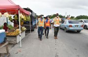 Minister of Public Works, Juan Edghill and other officials pass by a fruit vendor with her temporary vending stall and motor truck that was set up behind the Botanical Gardens on Sheriff Street on Saturday (Elvin Croker photo)